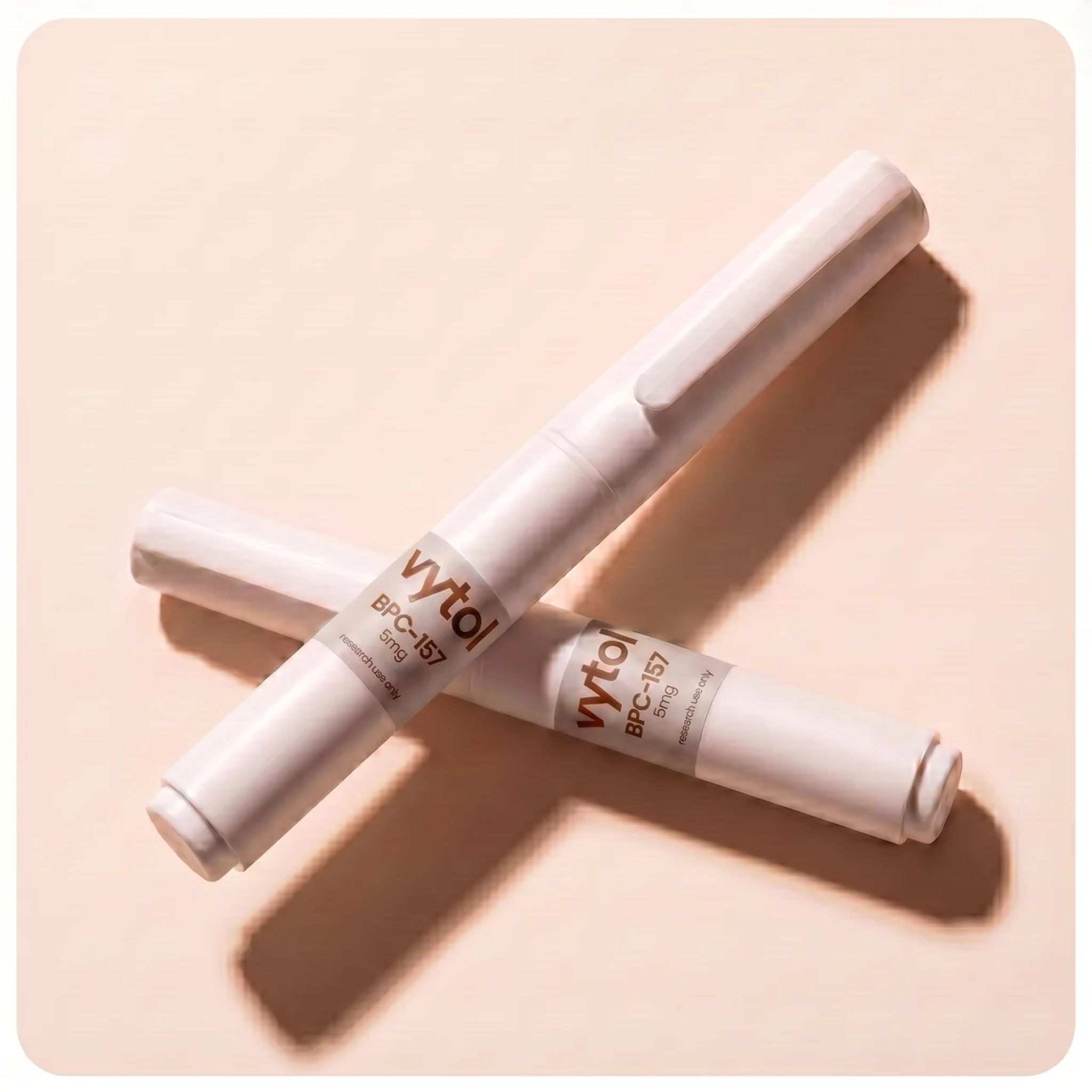 Two Vytol BPC-157 10mg research pens crossed in X formation, white injection pens with branded labels, cream background, editorial product photography